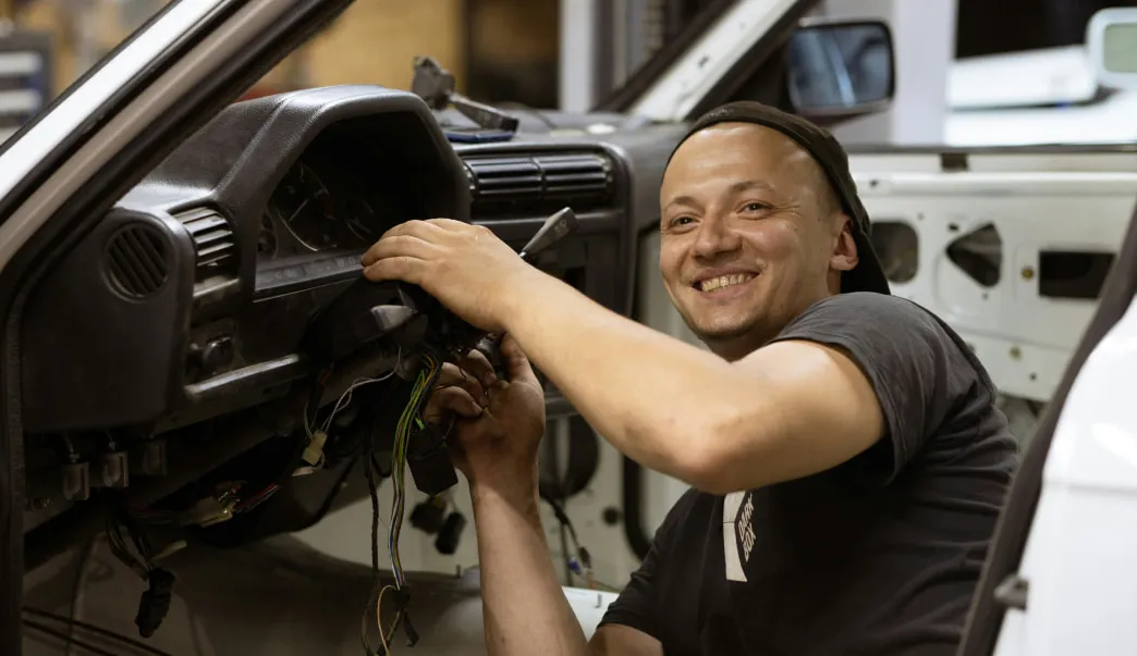 Foto de um homem consertando um carro e sorrindo para a câmera